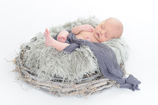 Newborn-Baby-liegt-auf-mit-Fell-bedecktem-Weidenkranz
