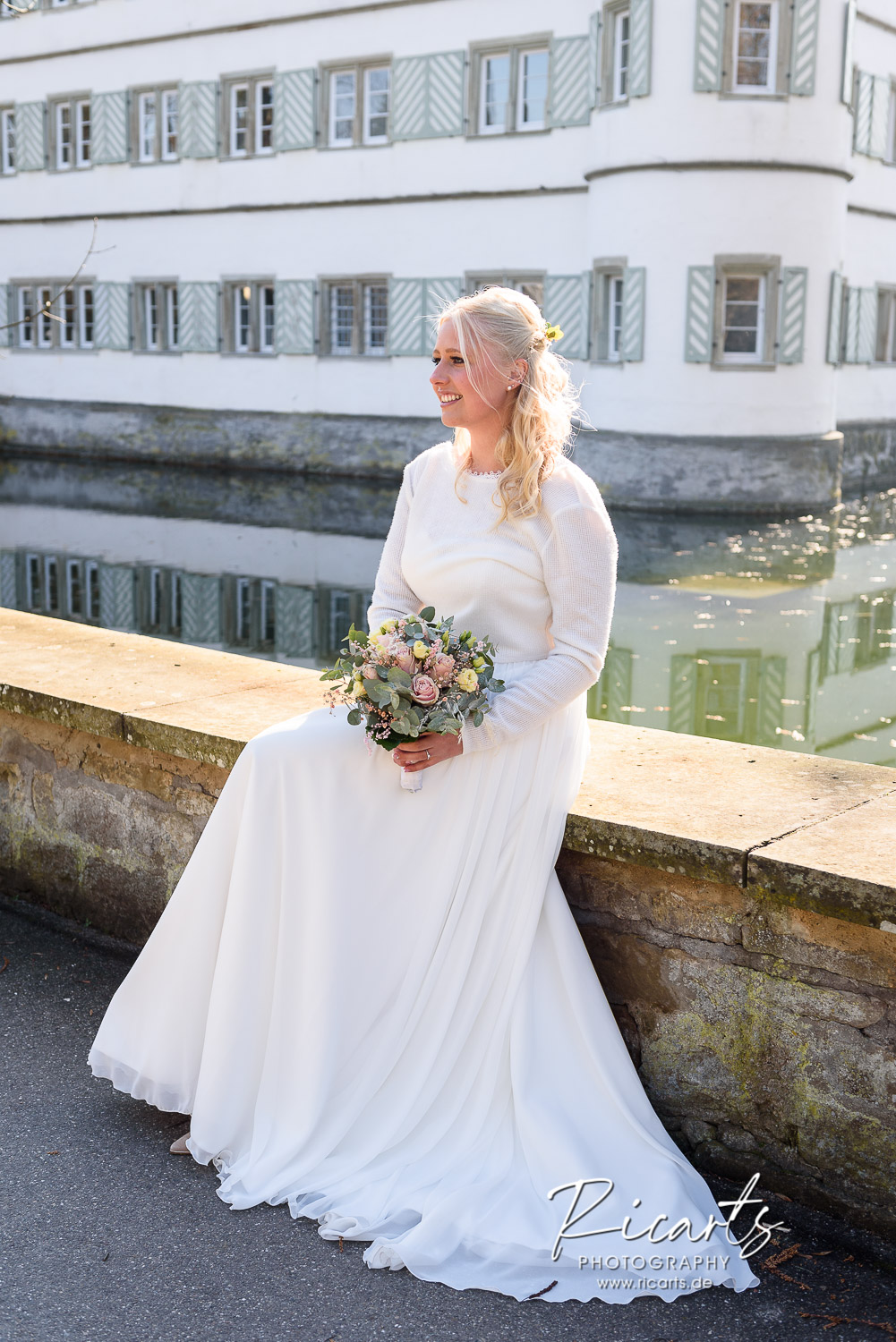 Braut-sitzt-auf-Mauer-vor-Wasserschloss