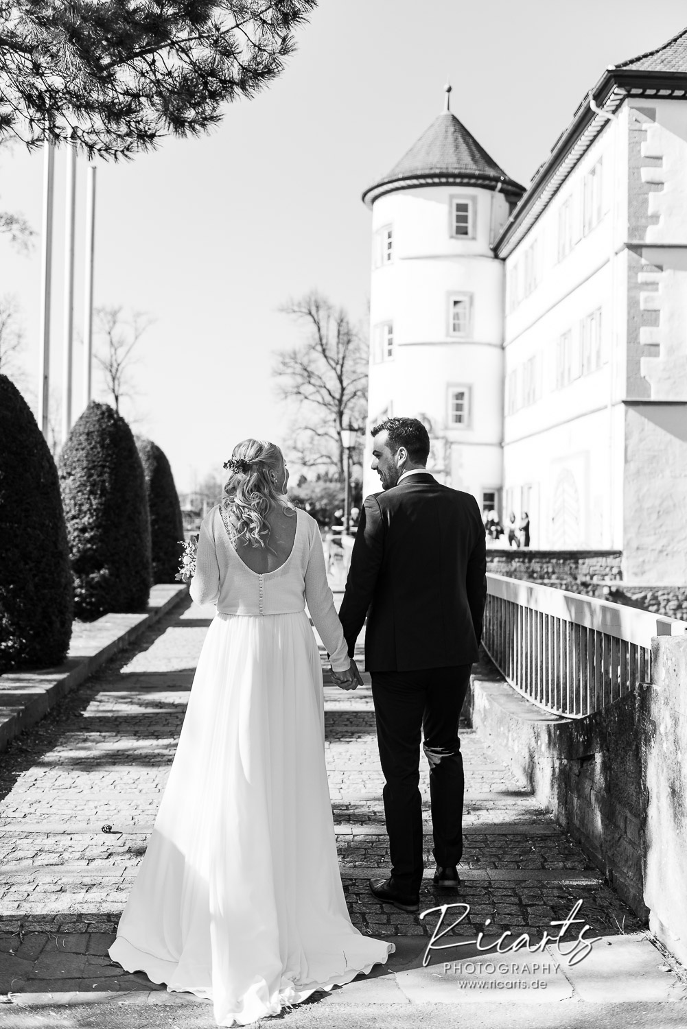 Brautpaar-geht-hand-in-hand-auf-Wasserschloss-zu