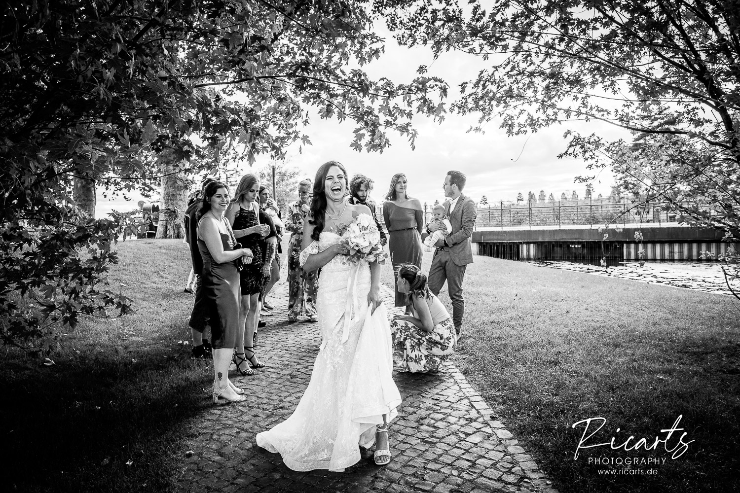 Braut-steht-lachend-mit-Hochzeitsgästen-unter-einem-Baum