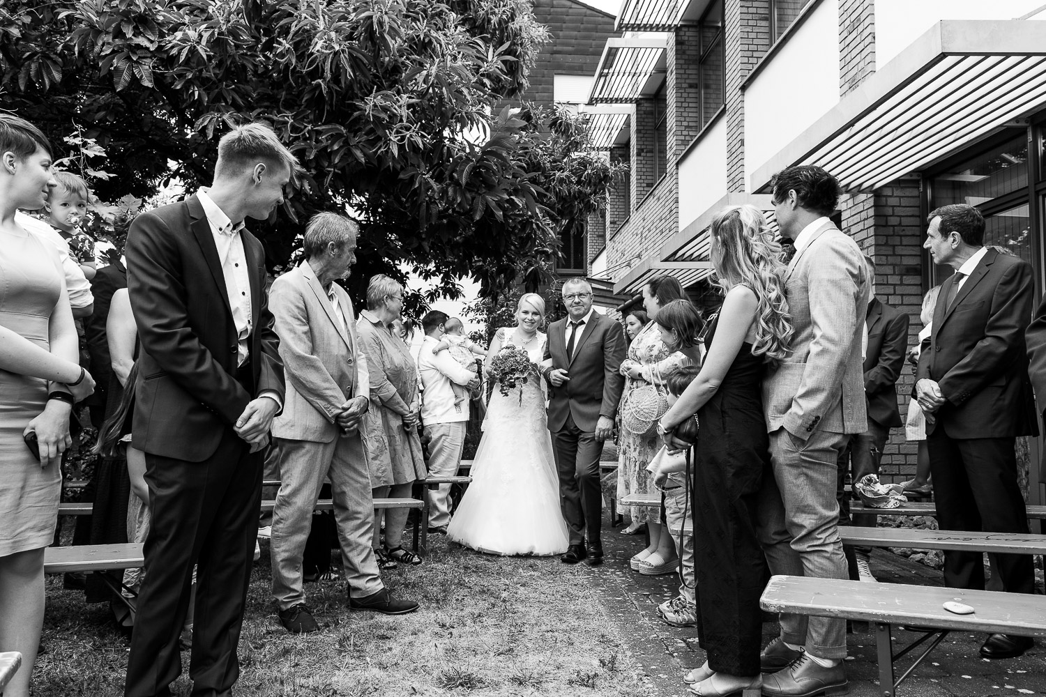 Brautvater-führt-Braut-zum-wartenden-Bräutigam-umringt-von-Hochzeitsgesellschaft