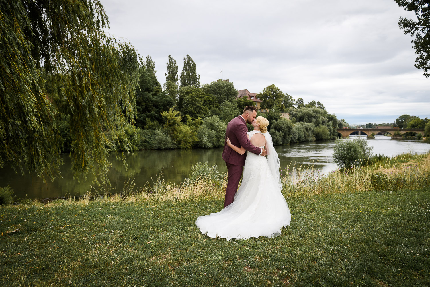 Brautpaar-von-Hinten-steht-am-Flussufer-und-küsst-sich