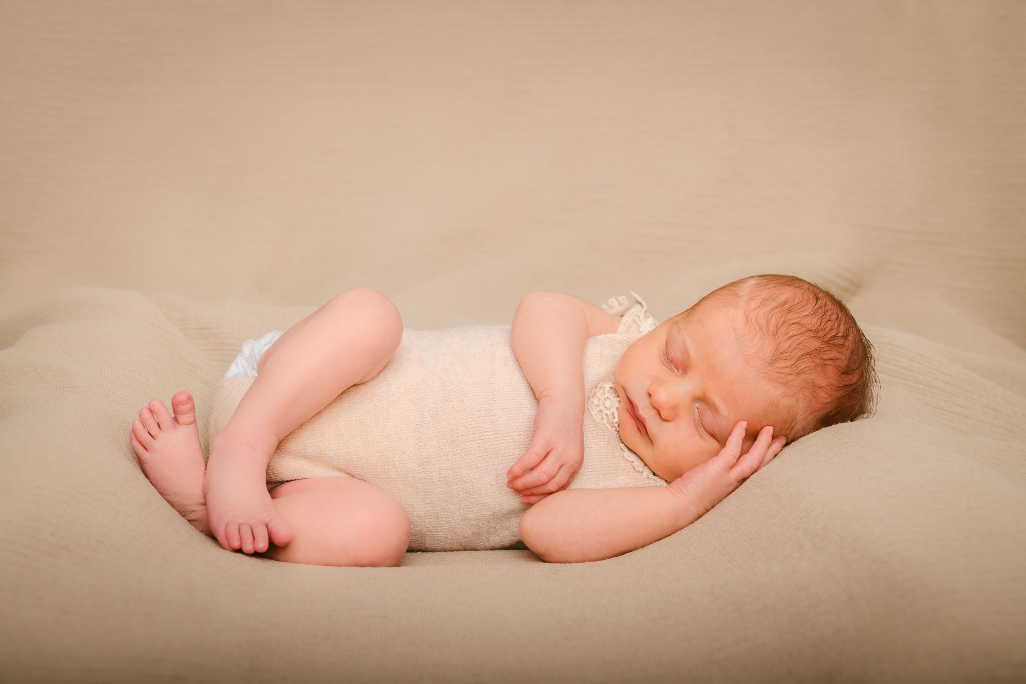 Newborn-Baby liegt schlafend auf einem beige-farbenen Kissen